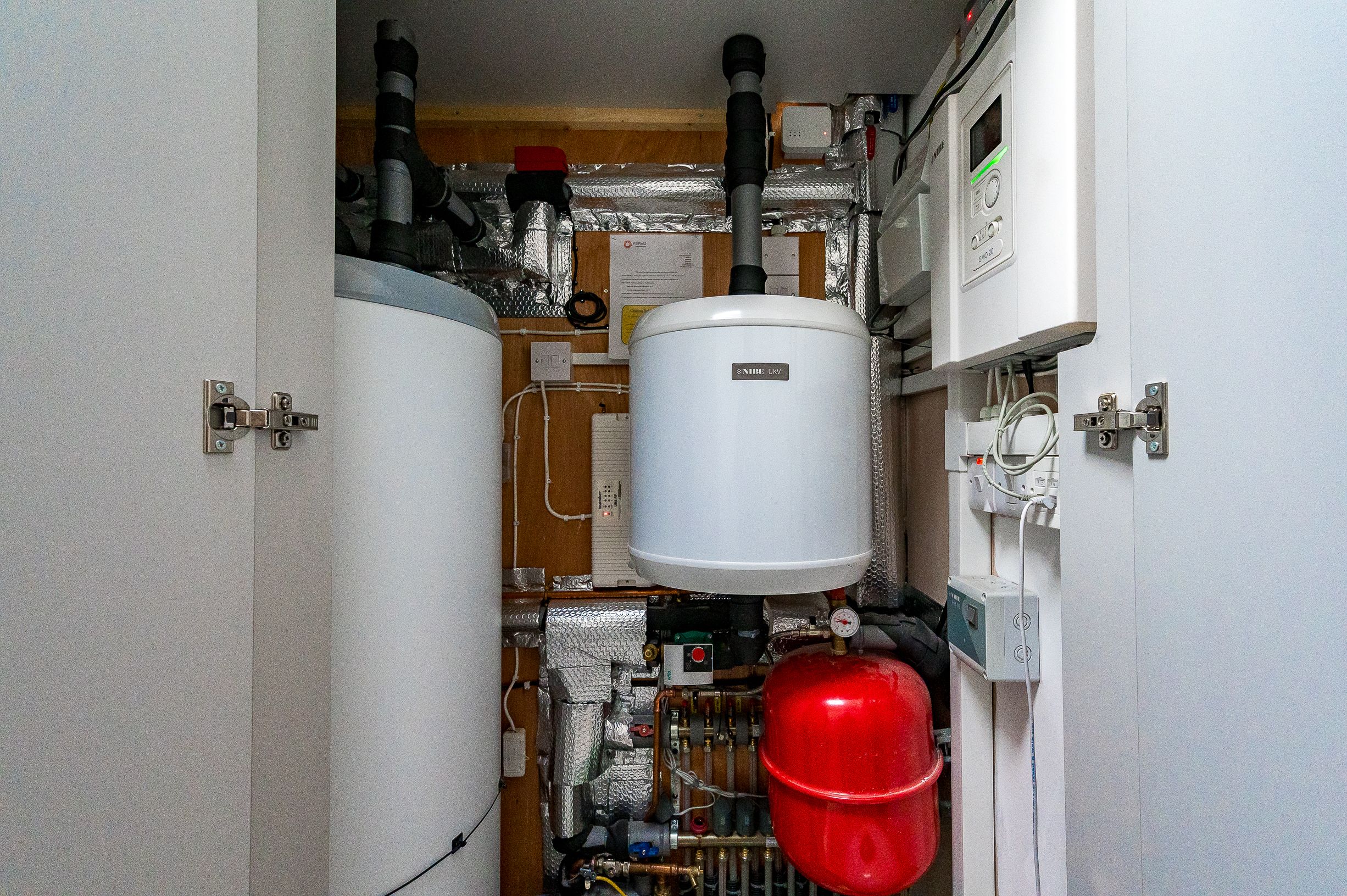 A red boiler and 2 silver water tanks in a retrofitted home