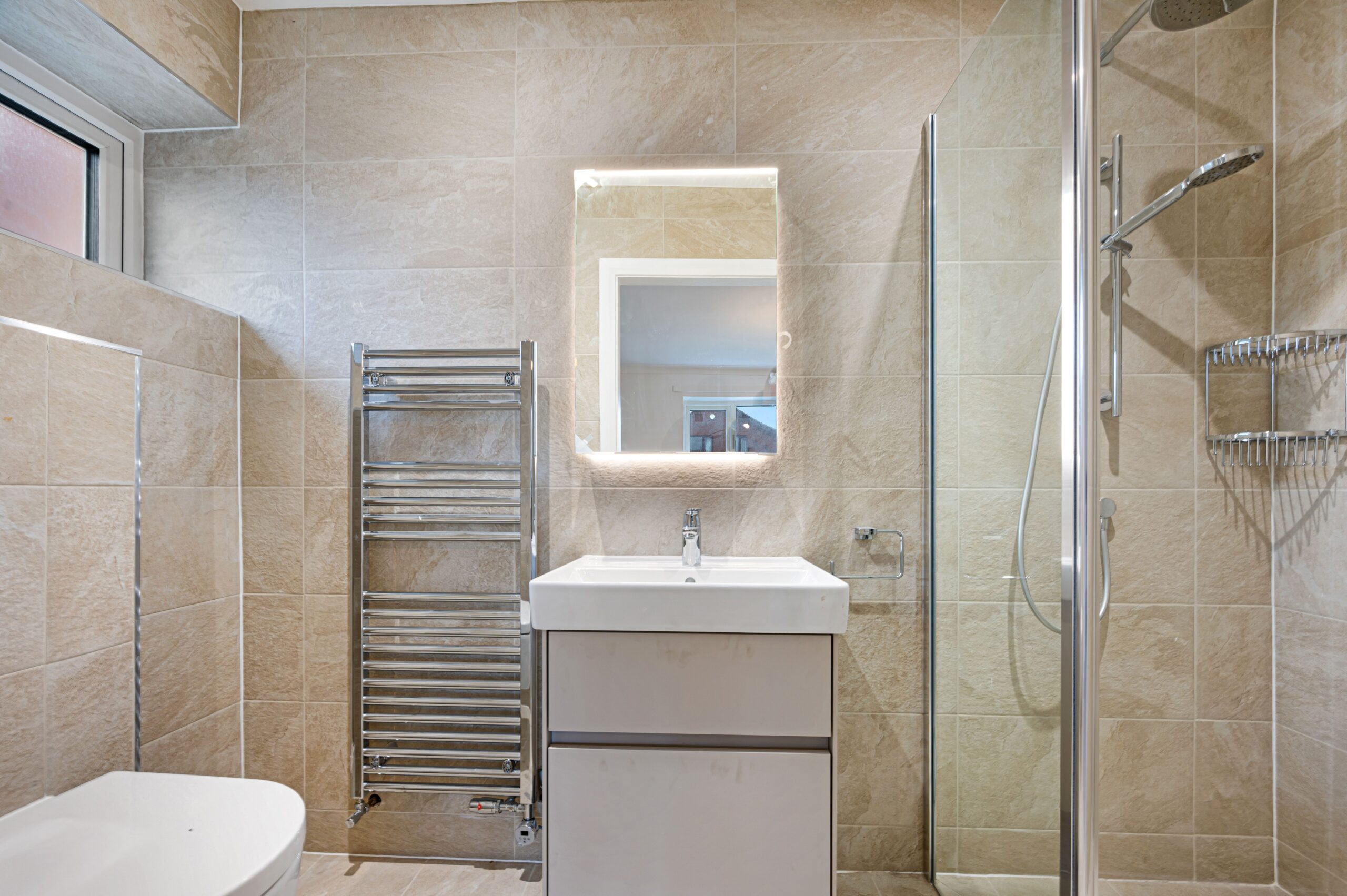 An en-suite bathroom within the master bedroom of the retrofitted bungalow, showing a shower, toilet, sink and LED mirror