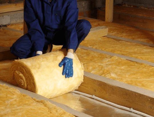 An imagine of a working man in a blue jumpsuit rolling out loft insulation